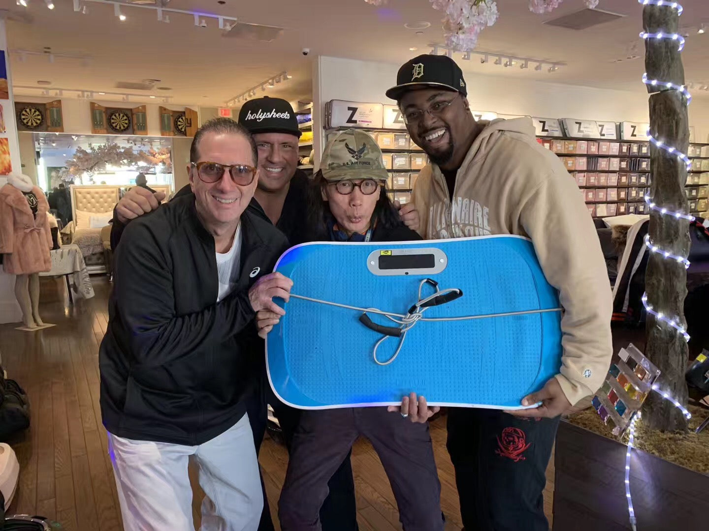 Four people posing together in a retail store, holding a bright blue textured fitness board with a white handlebar and attached black straps.